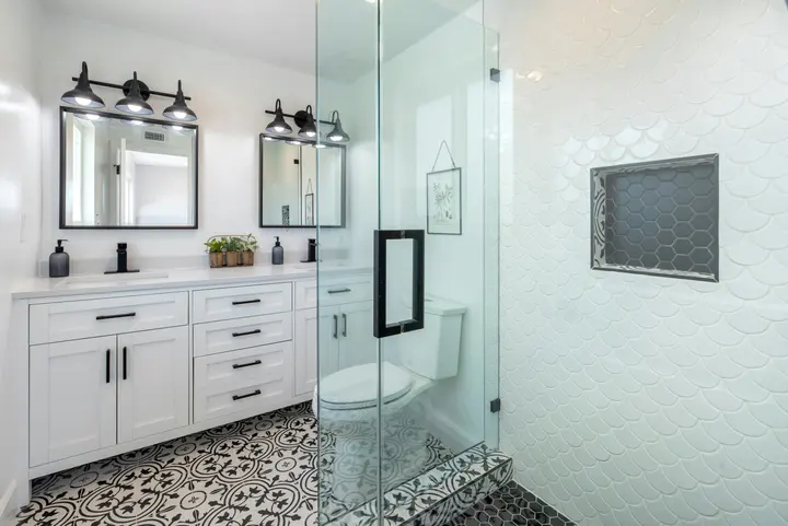 Bathroom with a scalloped tile shower wall, hexagon niche, patterned floor tile and double vanity
