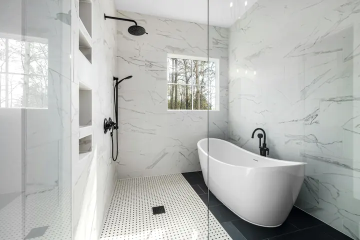 Freestanding tub on a dark tile floor beside a marble-look glass shower