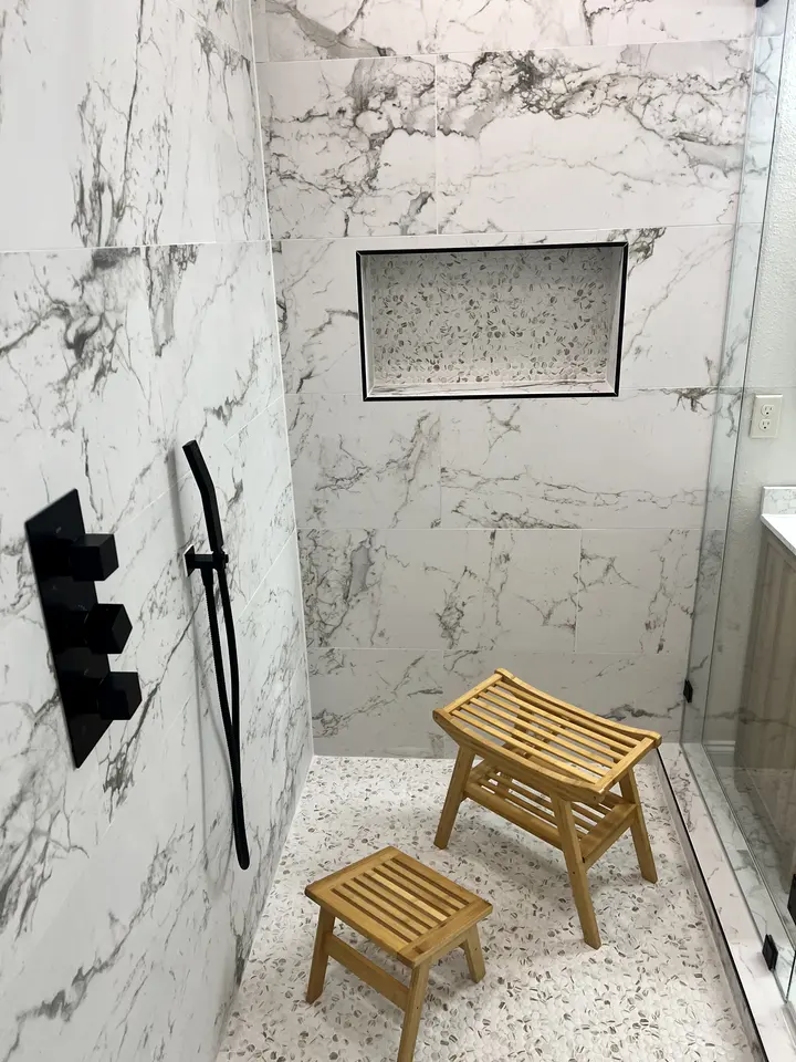 Marble-look shower with a matte black valve trim, speckled floor and teak benches