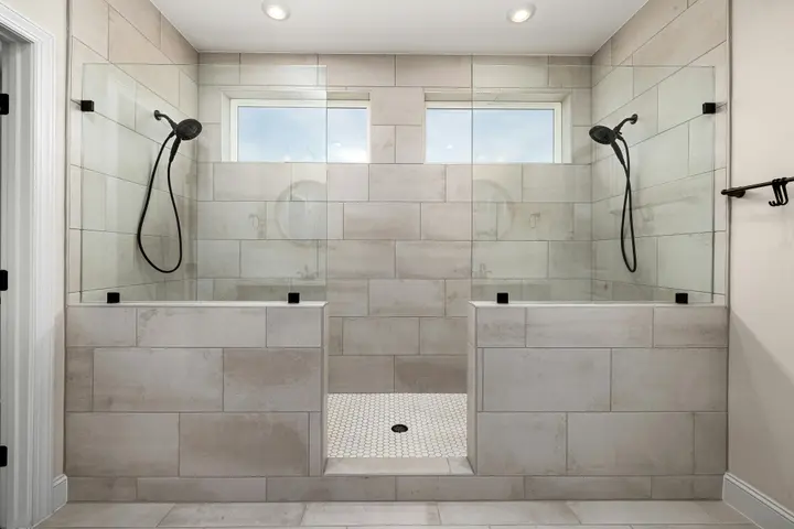 Double walk-in shower with two shower heads, tiled half walls and twin windows
